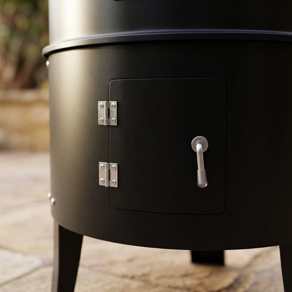 Close-up of a hinged steel access door with its latch on the black smoker body